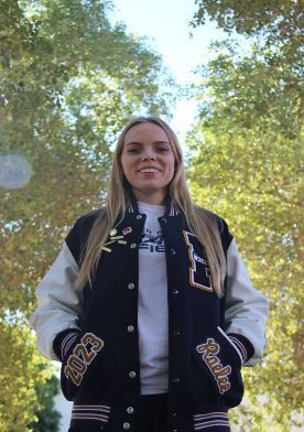 Raelee Merritt in her letter jacket flanked by leafy green trees